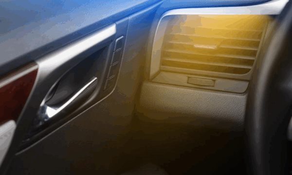 Close-up of a car’s interior showing the air vent, door handle, and dashboard, with a yellow light glare partially covering the image.
