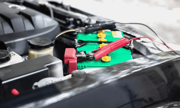 A red jumper cable clamp attached to the positive terminal of a car battery.