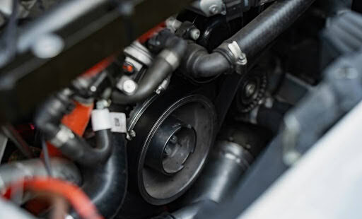 Close-up view of a car engine, showing various black hoses, metal components, and a belt pulley, highlighting the inner mechanical parts and details.